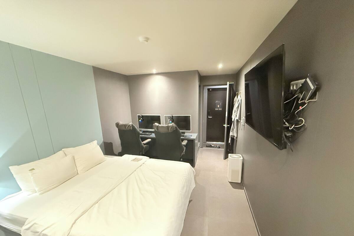 A modern hotel room with a large bed, a desk with a computer, a mirror, and a wardrobe.