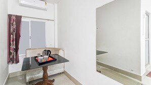 Ett litet rum med ett bord, en stol, ett fönster med gardiner och en luftkonditioneringsanläggning.