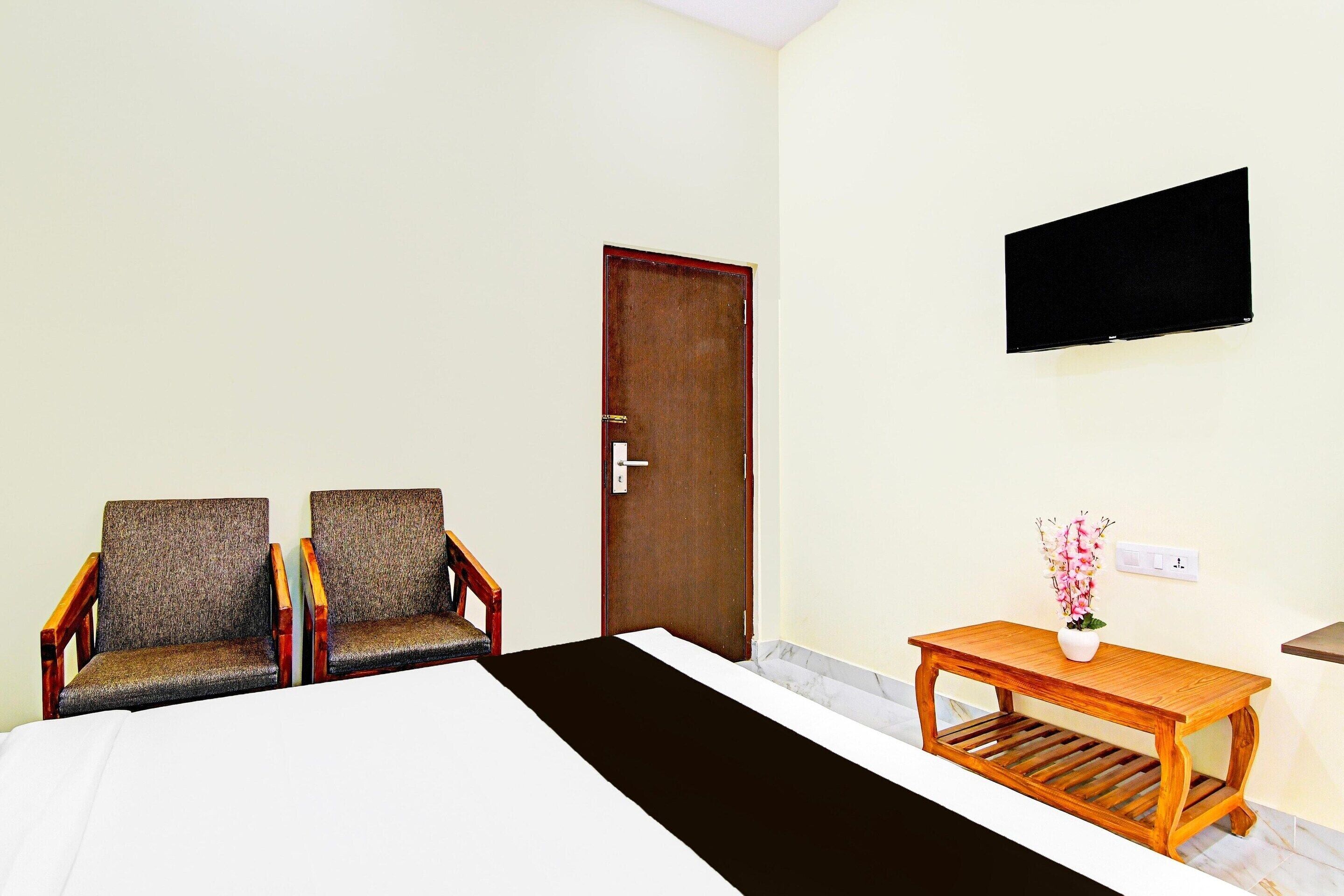 Une chambre d’hôtel avec deux fauteuils, une table en bois, un lit, une porte et un téléviseur fix é au mur.