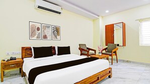Habitación de hotel con una cama, dos sillas, una mesita de noche, aire acondicionado y decoración en la pared.