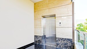 Un ascensor moderno con detalles metálicos, una pared de mármol y una barandilla de vidrio.