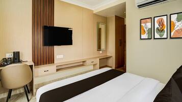 A hotel room with a bed, a desk with a chair, a flat-screen TV, a mirror, and artwork on the wall.