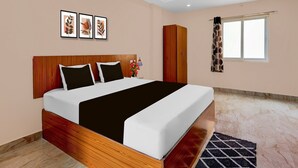 A bedroom with a wooden bed, a wardrobe, a window with curtains, and framed artwork on the wall. - Deluxe Bheemili Beach Visakhapatnam (Bhimunipatnam)