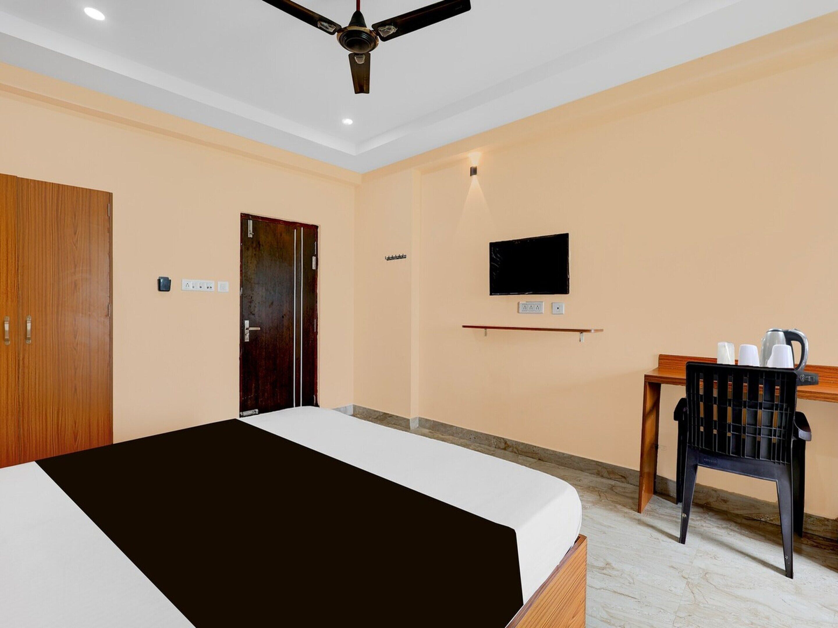 A hotel room with a bed, a desk, a chair, a television, and a ceiling fan.