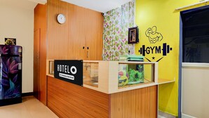A hotel reception desk with a wooden finish, a clock, a framed picture, and a wall with a gym logo. - Deluxe Bheemili Beach Visakhapatnam (Bhimunipatnam)