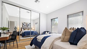 Un dormitorio moderno con una cama grande, un escritorio y una silla. Hay un ventanal corredera que da a otra habitación.