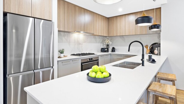 Una cocina moderna con electrodomésticos de acero inoxidable, armarios de madera, una encimera blanca y una isla central con un bol de manzanas.