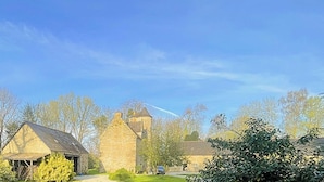 A stone building with a thatched-roof structure, surrounded by trees and greenery.