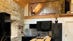 A kitchen with stone walls, a wooden ceiling, and a mezzanine with a chair.