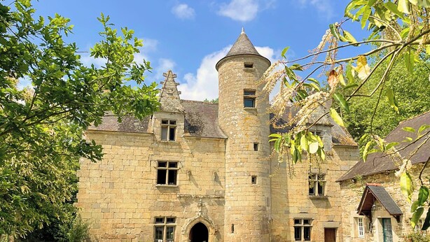 A historic stone building with a central tower, multiple windows, and a small entrance.
