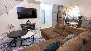 A living room with a sofa, a TV, a small table, and a kitchen in the background. - Unique GeoDome - Half Block to Beach (South Padre Island)