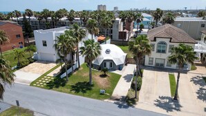 Zona residencial amb un edifici de forma arrodonida envoltat de palmeres i una vista despejada de l'oceà.
