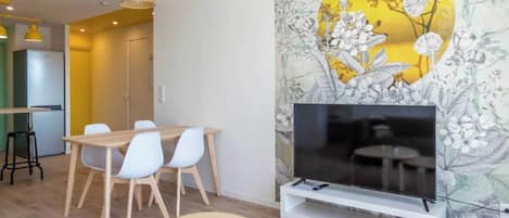 Una sala moderna con comedor, un televisor de pantalla plana sobre un mueble bajo y un papel tapiz floral.