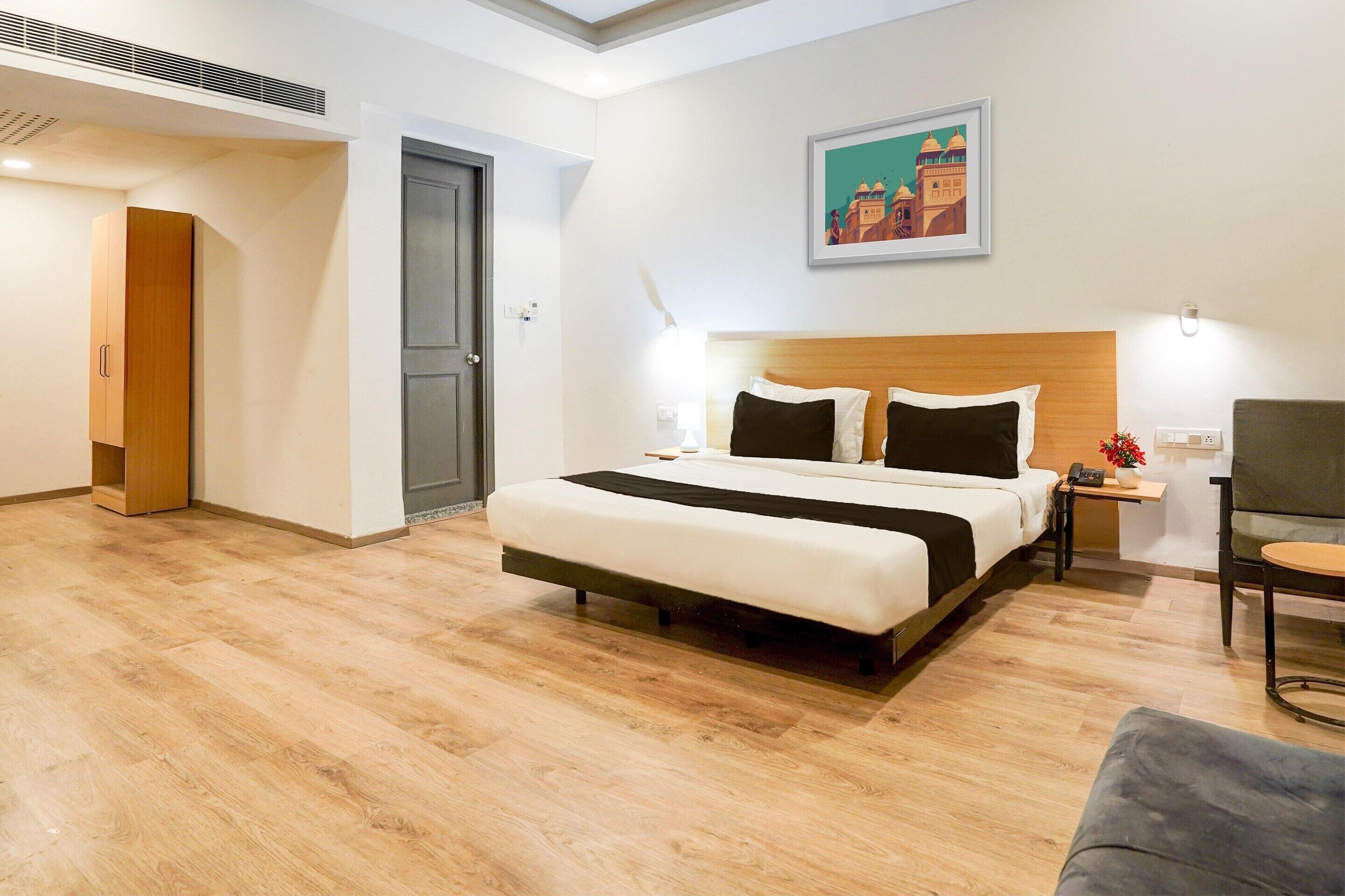 A hotel room with a bed, bedside table, chair, and a painting on the wall.