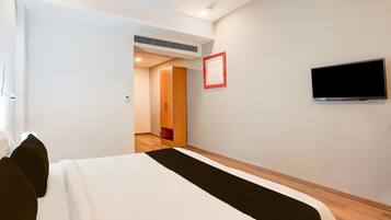 A hotel room with a bed, a flat-screen TV, a framed picture on the wall, and a wooden wardrobe.