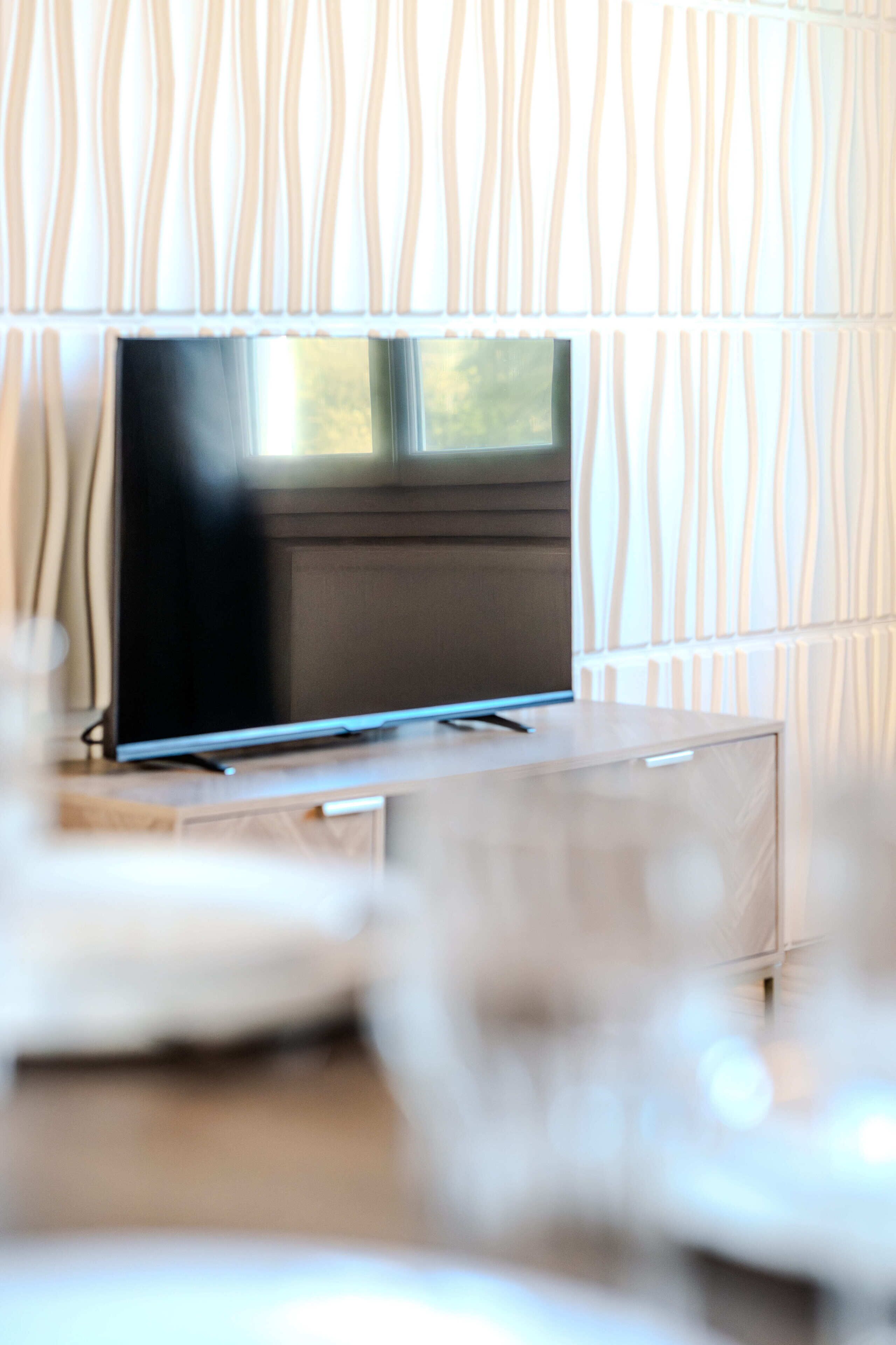 A flat-screen TV on a wooden stand in a room with patterned wallpaper.