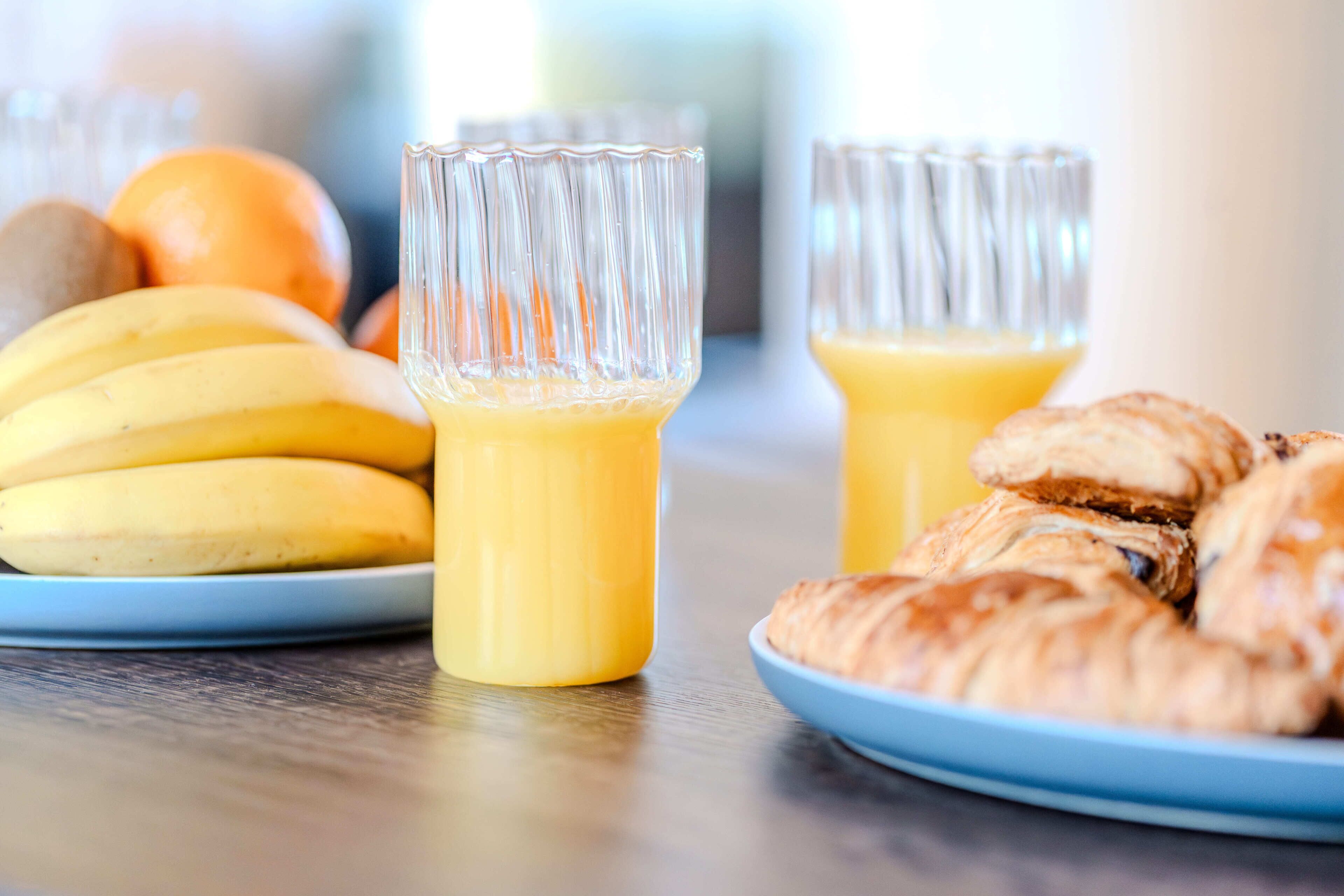 Desayuno con plátanos, croissants y jugo de naranja en platos.