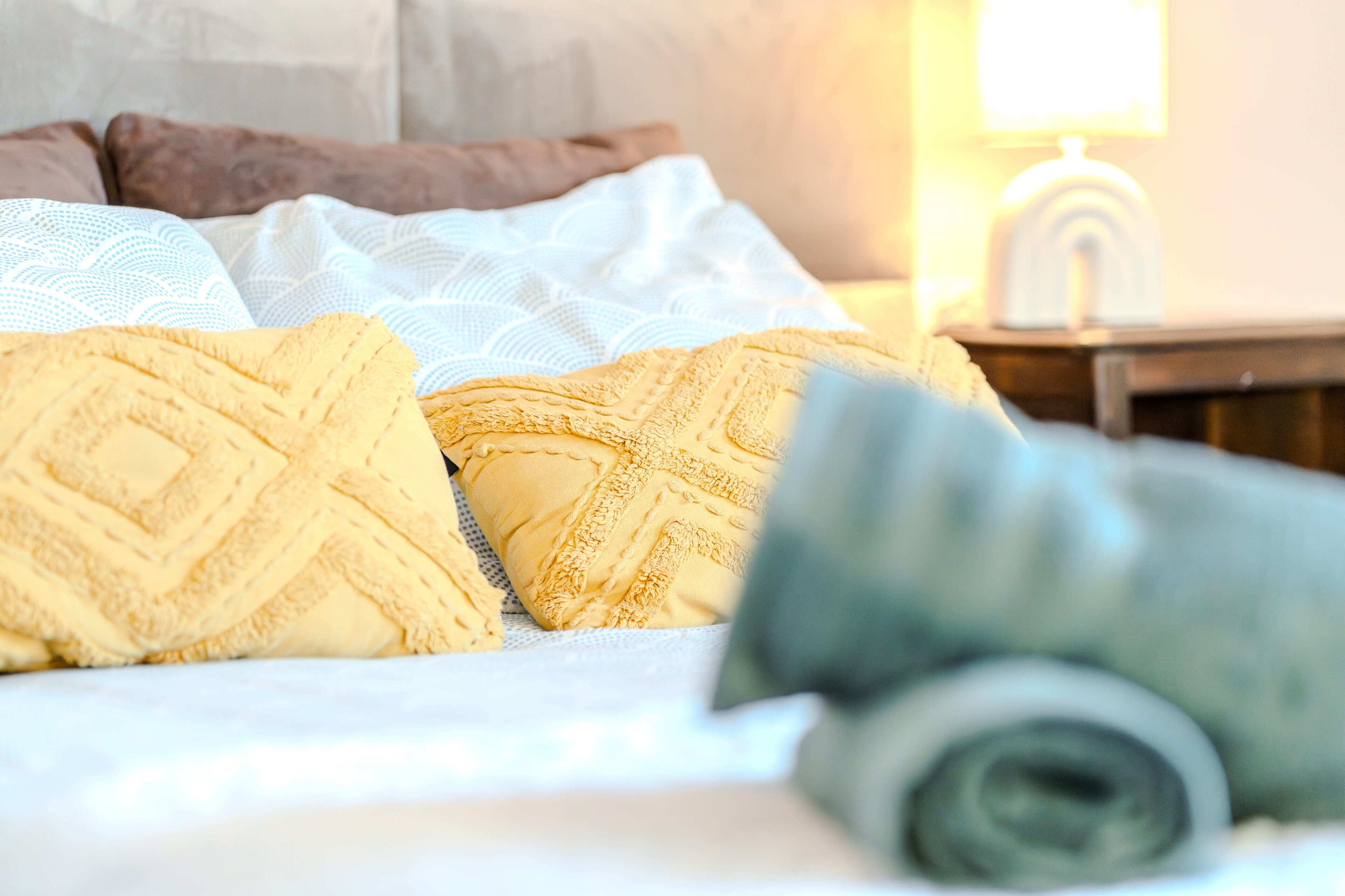A bed with patterned pillows and a rolled-up blanket.