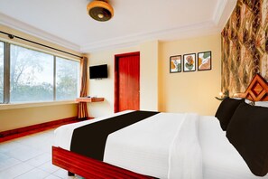 Une chambre d’hôtel avec un grand lit, une télévision, une porte rouge et une fenêtre donnant sur des arbres.