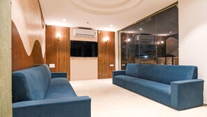A modern waiting area with two blue sofas, wooden paneling, an air conditioning unit, and a glass partition. - Deluxe Pallette Shree Jagannatha Puri Lotus (Puri)