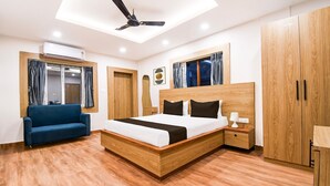 A modern bedroom with a wooden bed, a blue sofa, and a ceiling fan. - Deluxe Pallette Shree Jagannatha Puri Lotus (Puri)