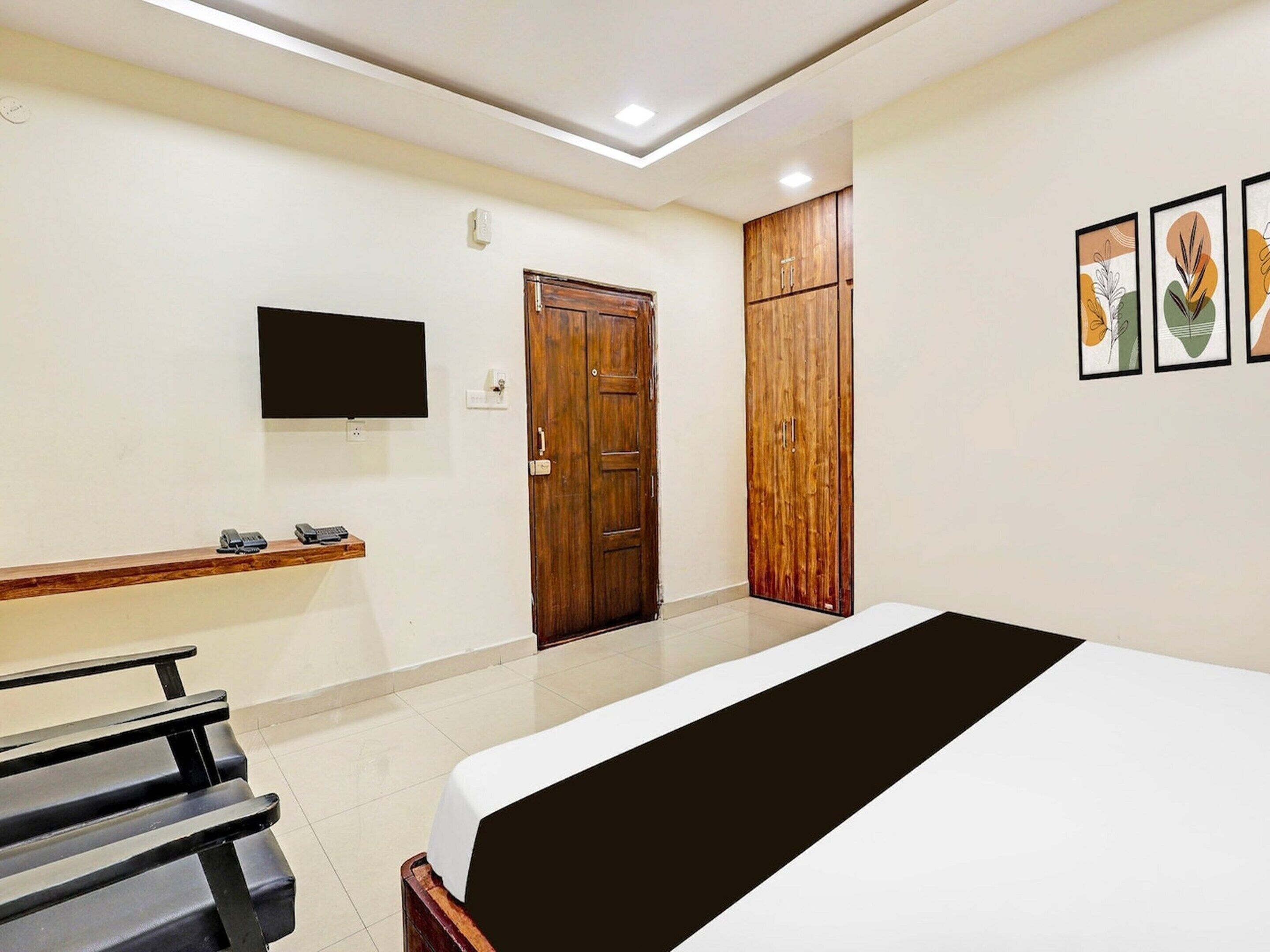 Een hotelkamer met een bed, een aan de muur bevestigde televisie, een houten garderobe en een bankje met telefoon en afstandsbediening.