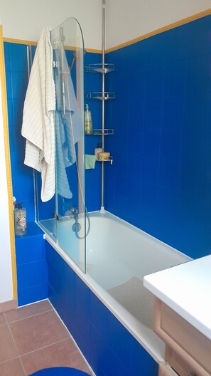 Et badeværelse med en glasafskærmet brusekabine, et hvidt badekar og blå fliserede vægge.