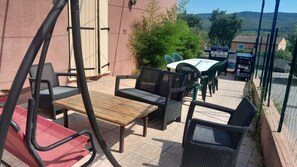 En udendørs terrasse med fletmøbler, et træbord og udsigt over et landligt landskab.