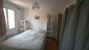 Et soveværelse med seng, garderobeskab, natbord, vægventilator og vindue.