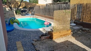 En baghave med swimmingpool, træterrasse og stenvæg.