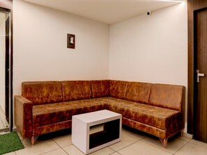 A corner living room with a brown sofa, a white coffee table, and a small picture frame on the wall. - Premiumnana Chiloda Near Airport (Gandhinagar)