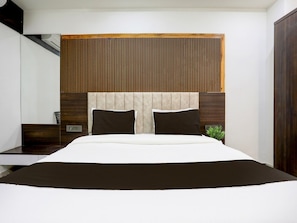 A modern bedroom with a bed, a nightstand, a mirror, and a wooden panel wall. - Premiumnana Chiloda Near Airport (Gandhinagar)