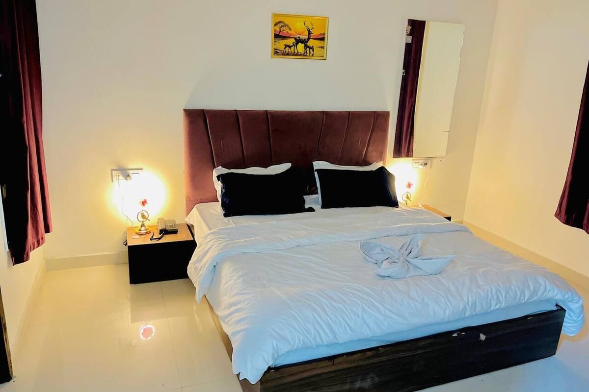 A neatly made bed with white linens, a wooden headboard, and a wall-mounted air conditioner.