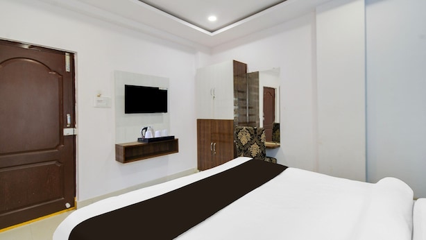 A hotel room with a bed, a TV mounted on the wall, a wooden wardrobe, and a mirror. - Deluxe Rks Prestige (Hyderabad)