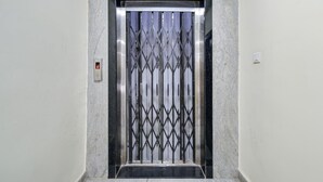 An elevator with a metal grille door, a control panel with a red light, and a marble wall. - Deluxe Rks Prestige (Hyderabad)
