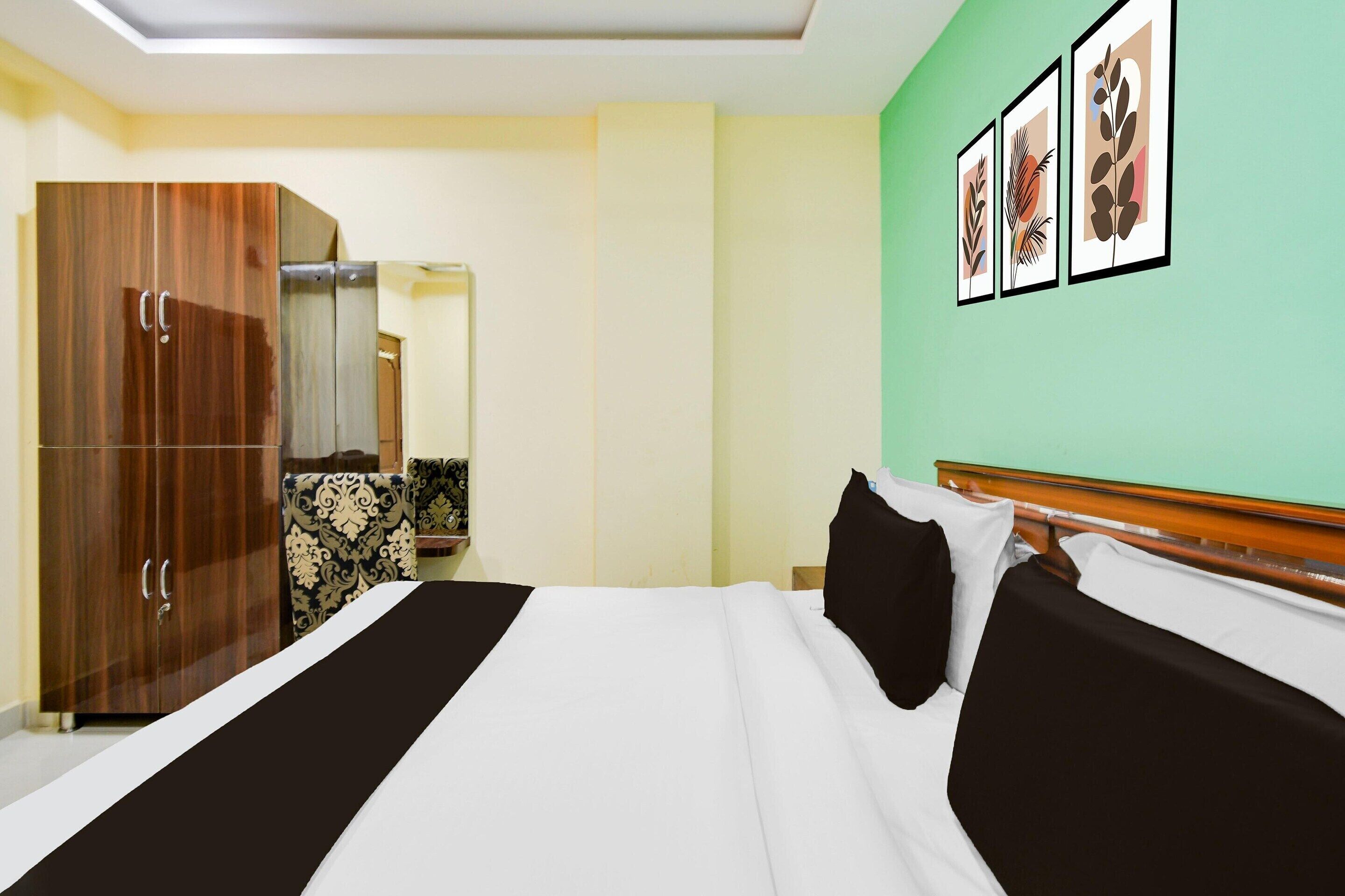 A hotel room with a bed, a wardrobe, a mirror, and framed artwork on the wall.