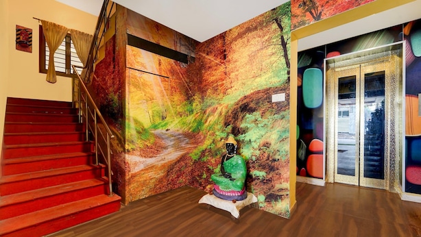 A staircase with red steps, a Buddha statue, and a mural with a forest scene. - Premium Hotel Apple Grand (Coimbatore)