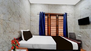 A hotel room with a bed, a TV, a window with curtains, a vase with flowers, and a chair. - Premium Hotel Apple Grand (Coimbatore)