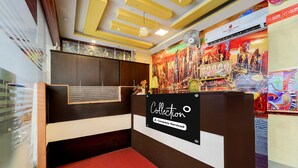 A reception desk with a 'Collection' sign, a cityscape mural, and a ceiling with yellow beams and a chandelier. - Premium Hotel Apple Grand (Coimbatore)