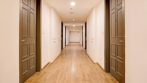 A long, narrow hallway with wooden flooring and dark wooden doors on both sides. - Super Deluxe Room Landmark Hotel (Lucknow)