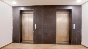 A pair of elevators with a dark tiled wall and a wooden floor. - Super Deluxe Room Landmark Hotel (Lucknow)