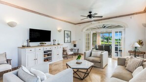 A spacious living area with a TV, white cabinetry, and a view through an arched doorway to an outdoor patio. - Sugar Hill Birds Eye Villa - by ZenBreak (Mount Standfast)