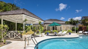 Un espace piscine avec des chaises longues, un coin salon abrité et des plantes en pot.