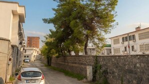 Una estrecha calle adoquinada con un coche estacionado, un muro de piedra y edificios a ambos lados.