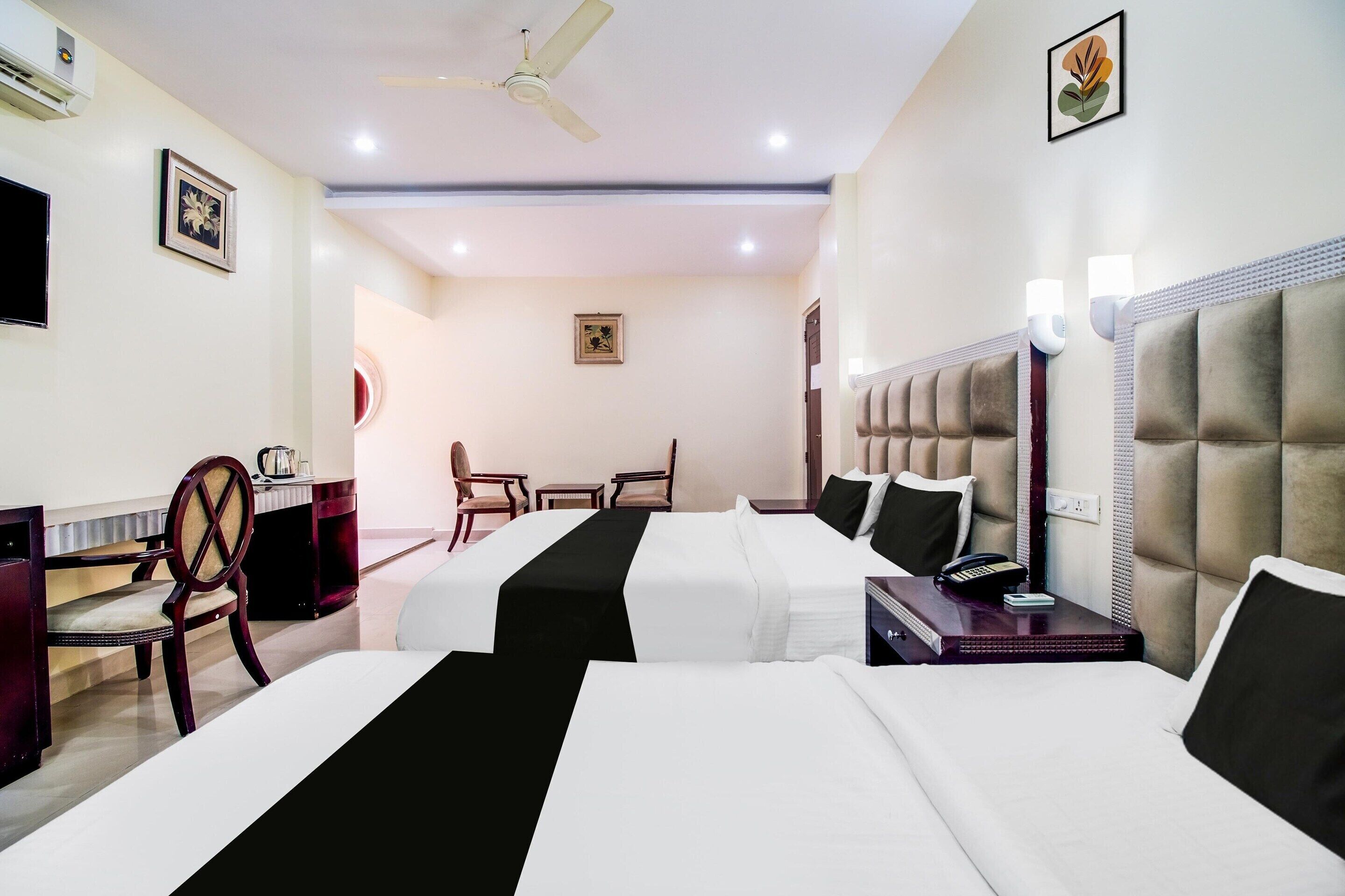 A hotel room with two beds, a desk, a chair, a ceiling fan, and wall-mounted lights.