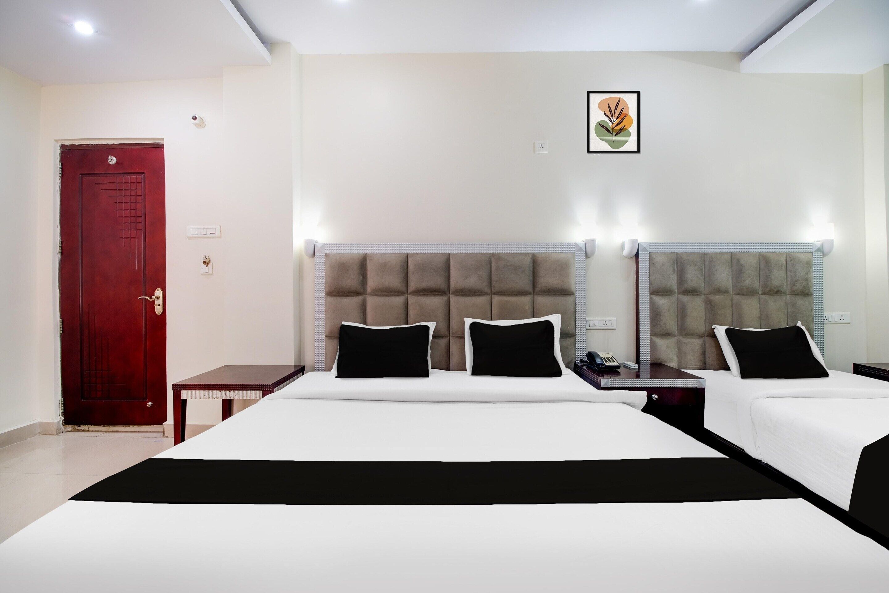 A hotel room with two beds, a red door, a small table, and a framed picture on the wall.