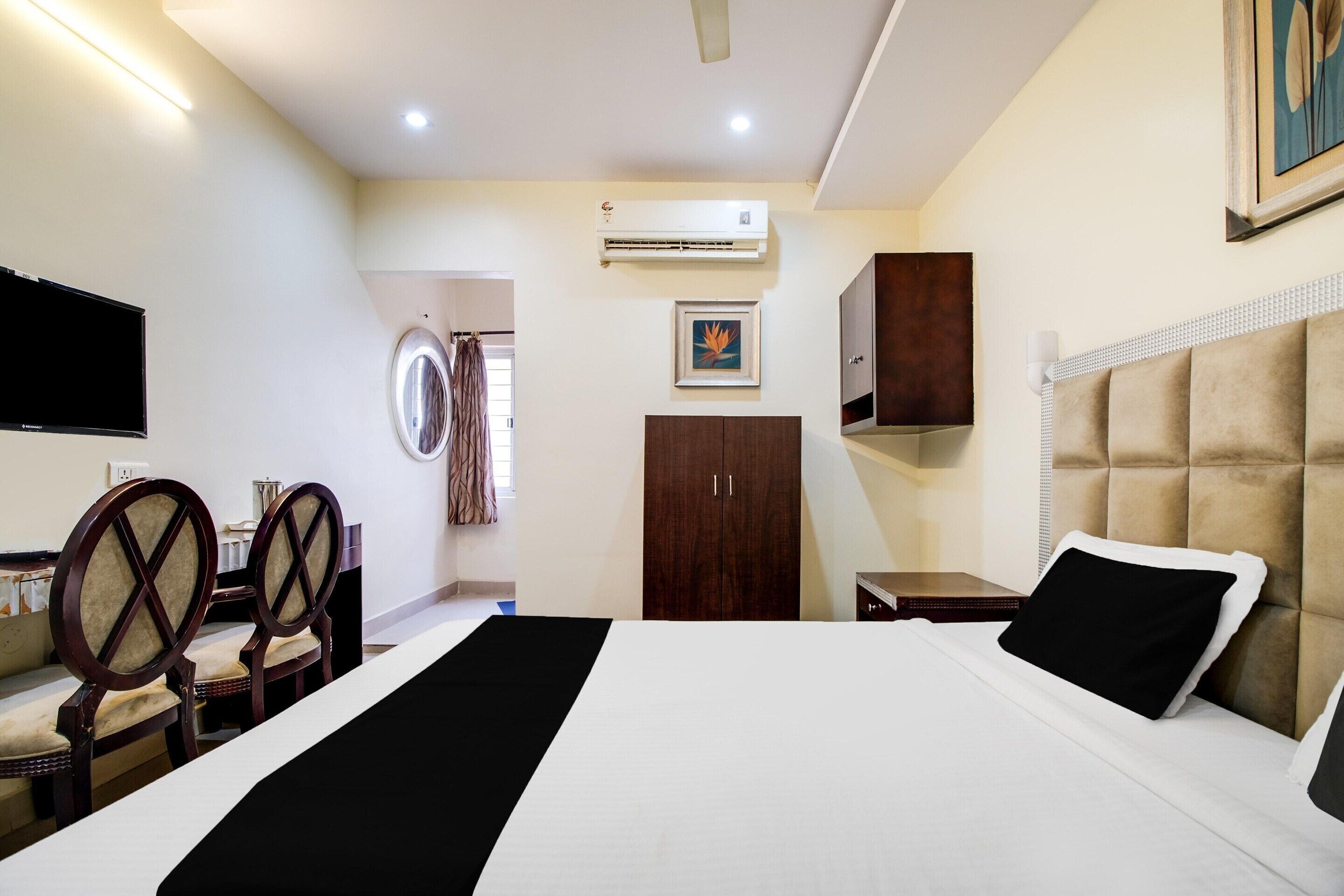 A hotel room with a bed, a desk with chairs, an air conditioning unit, a wardrobe, and a television.