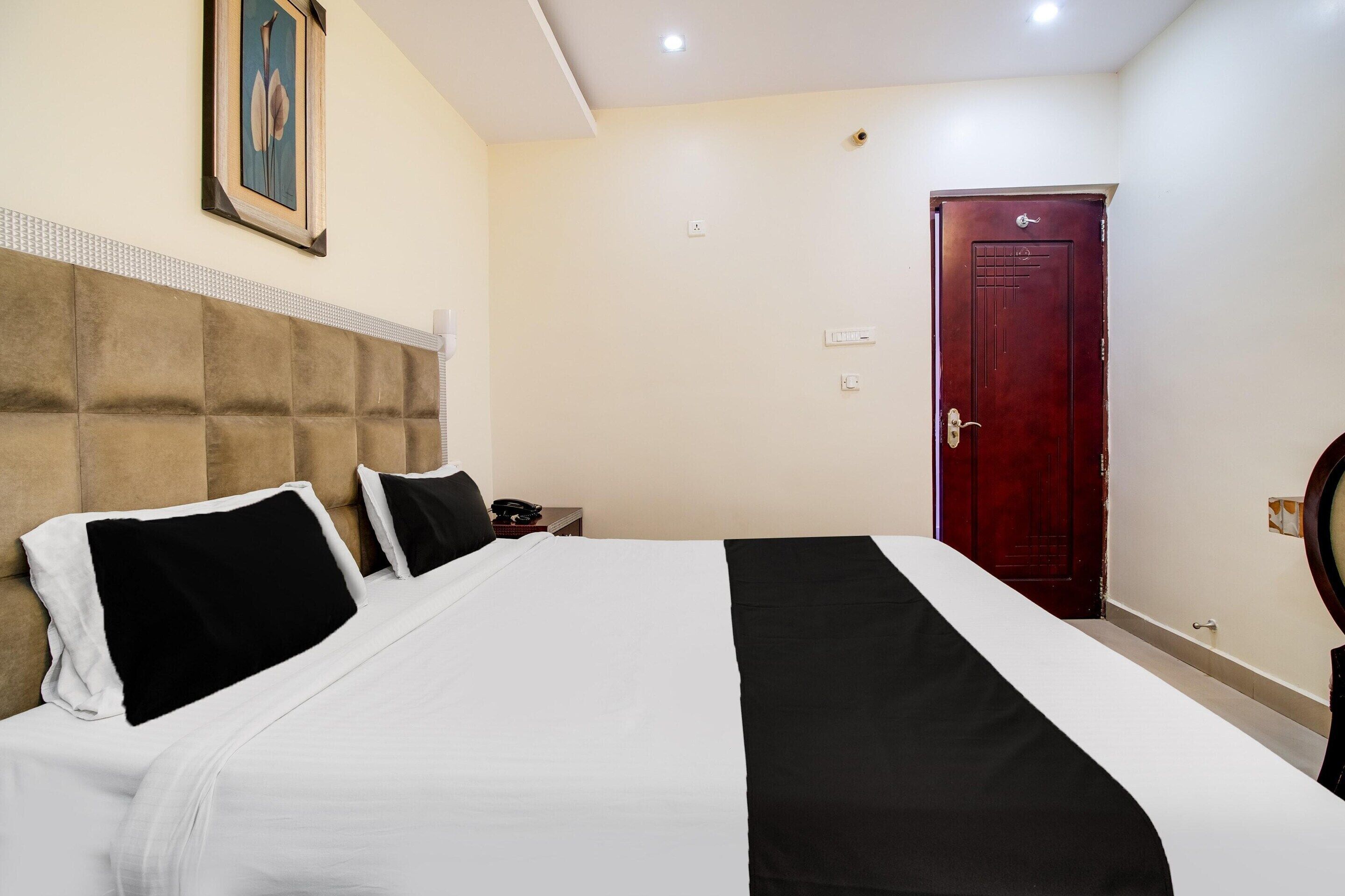 A hotel room with a large bed, a headboard, a red door, and a painting on the wall.