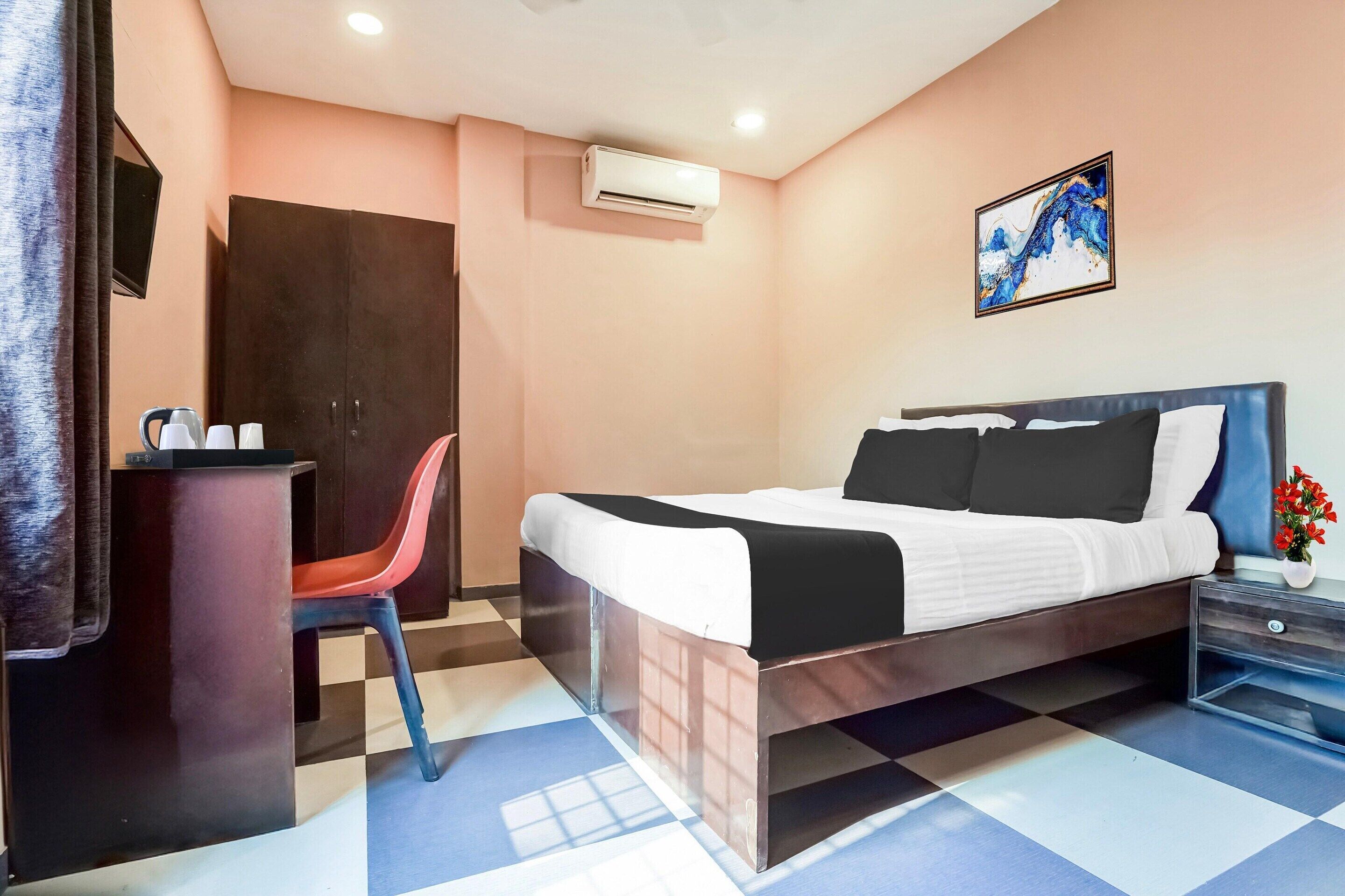 Een hotelkamer met een bed, een bureau, een stoel, een airconditioner en een schilderij aan de muur.