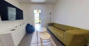 A modern living room with a sofa, a small table, a bean bag, and a TV mounted on the wall.